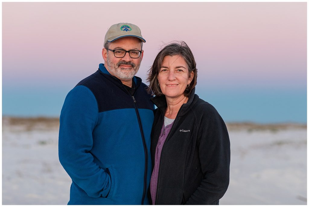 Older couple on Pensacola Beach during beautiful pink and purple sunset. Extended family photo sessions are a great way to document your vacation. Pensacola Beach Photographers