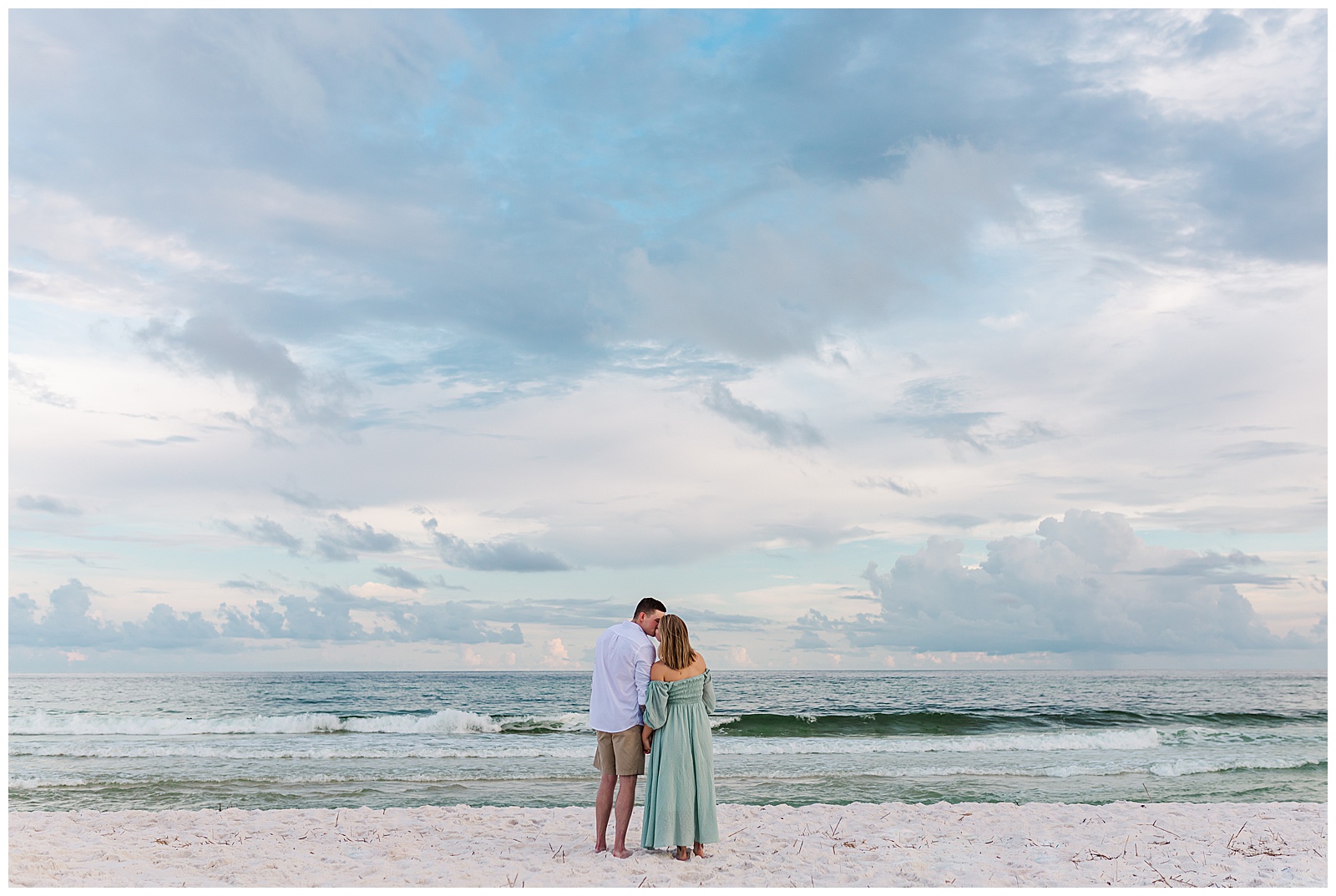 Engaged couple leaning in for a kiss at the waters edge on Pensacola Beach.