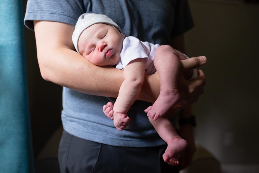Lifestyle newborn photography session with dad holding sleeping newborn son on his forearm.
