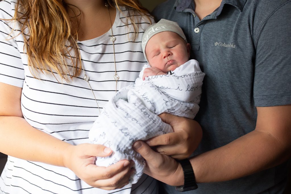 Mom and dad holding swaddled newborn son. 