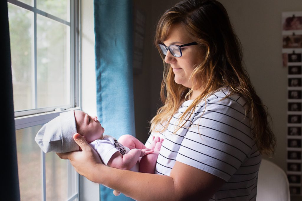 Lifestyle newborn photography session with mom holding newborn son by the window.
