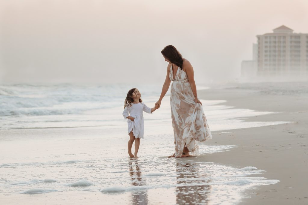 Mom and daughter walk down Pensacola Beach holding hands. 