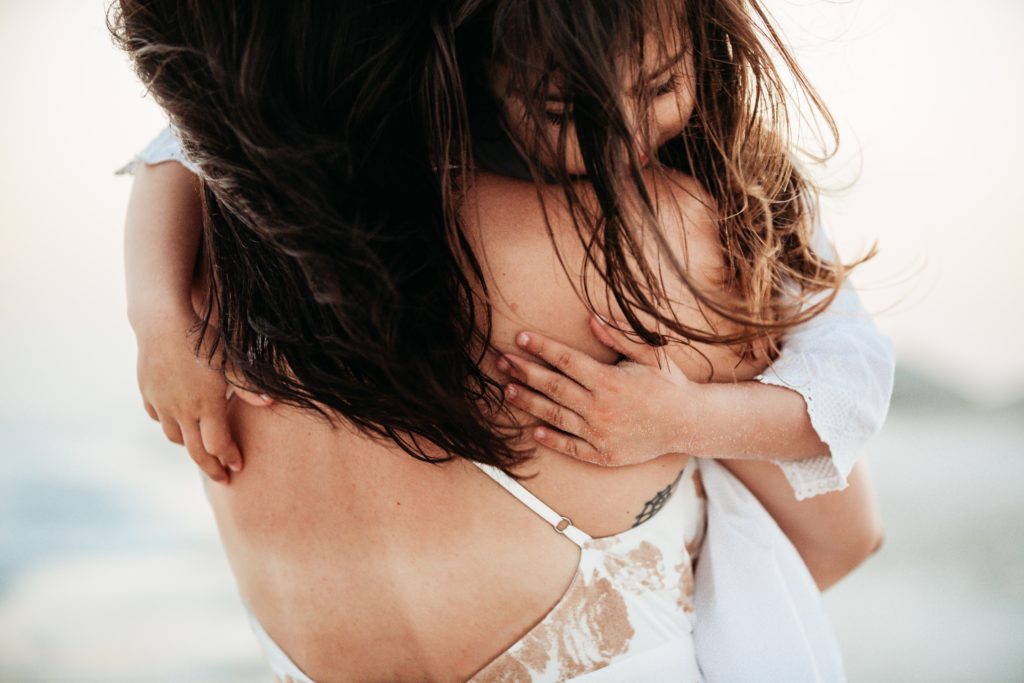Pensacola Beach vacation tips - wear sunscreen. Young daughter hugging mom on Pensacola Beach.