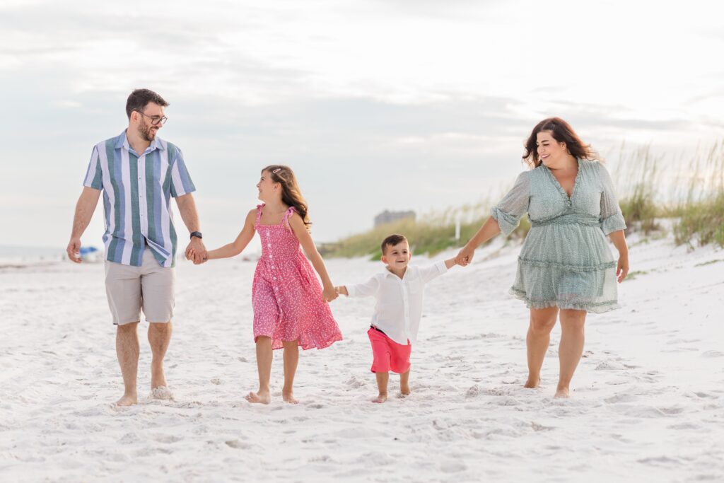 Family portrait session on Pensacola Beach with family of 4 walking down the beach holding hands. Photography by Jennifer Beal