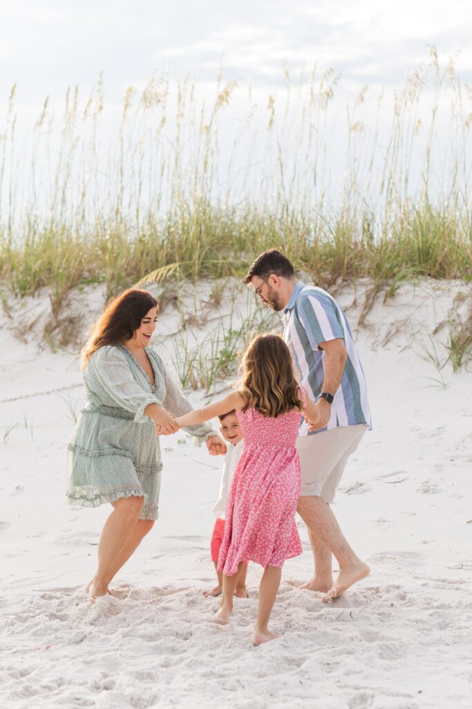 Family playing "Ring Around the Rosy" on the beach during a photo session with a photographer in Pensacola. Jennifer Beal Photography