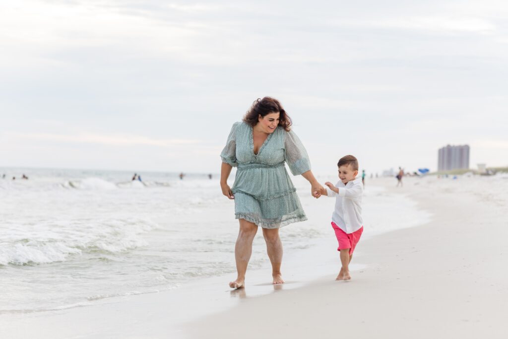 Mother and young son walking down Pensacola Beach at sunset. 