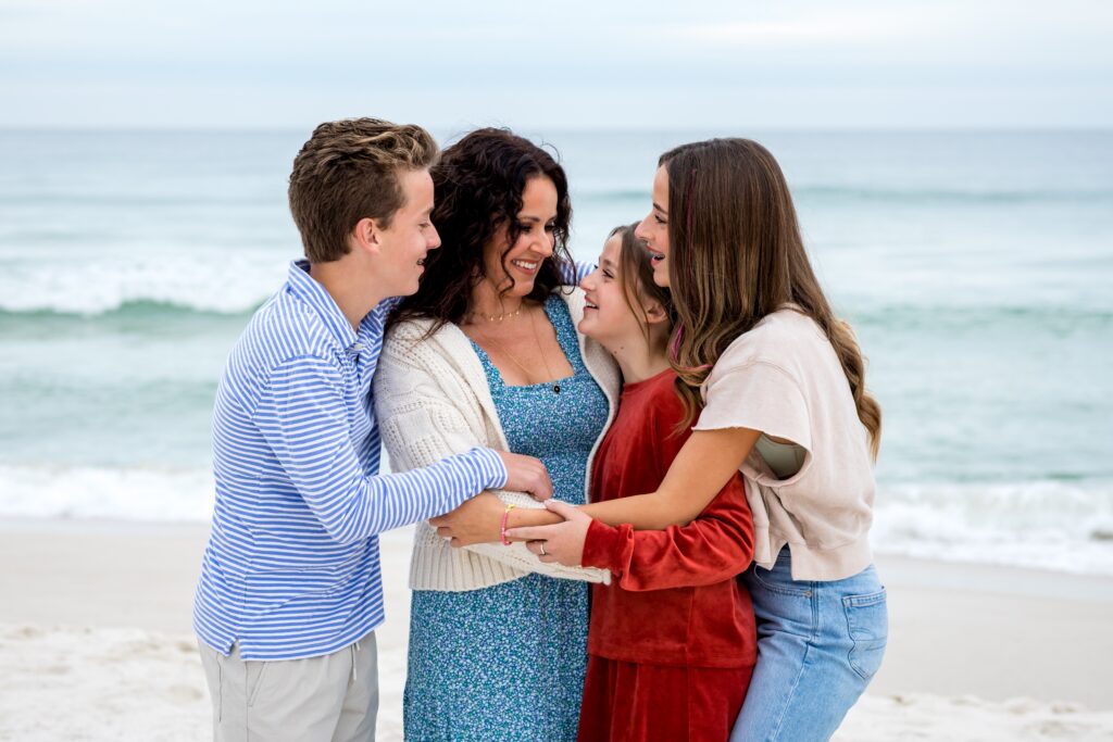 Pensacola Beach photography session with mom and three teenage children in group hug during family pictures on the beach.