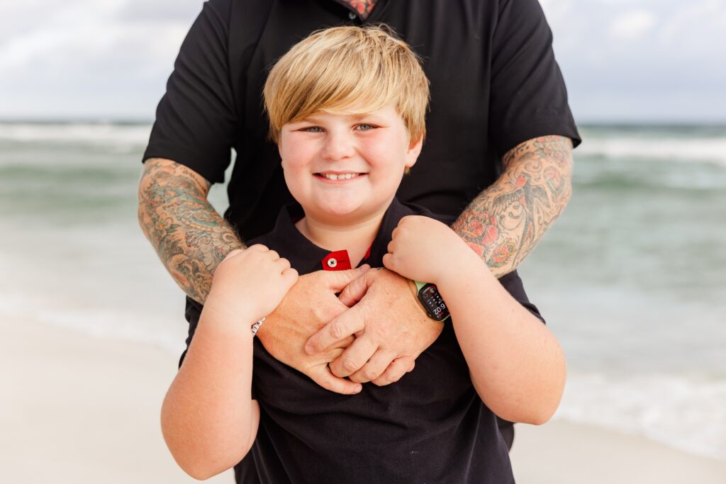 Family photo of son with dad's tattooed arms embracing him.