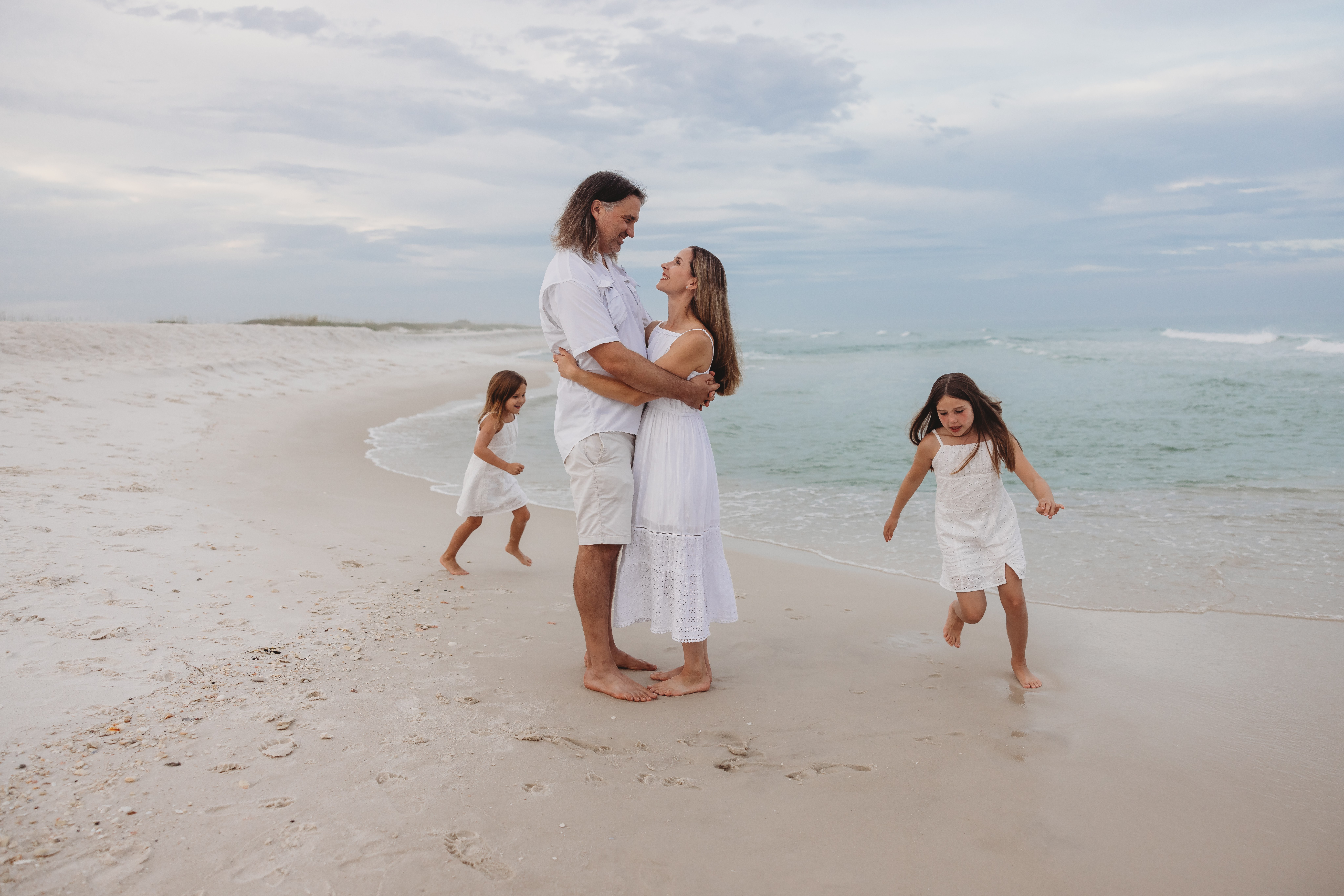 Young daughters run around parents during sunset at Navarre Beach. Family photo session on Navarre Beach by Jennifer Beal Photography.