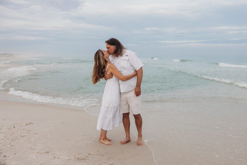 Couple in a slight dip as they kiss during sunset on Navarre Beach. Jennifer Beal Photography provides family beach photo sessions for vacationing families. 
