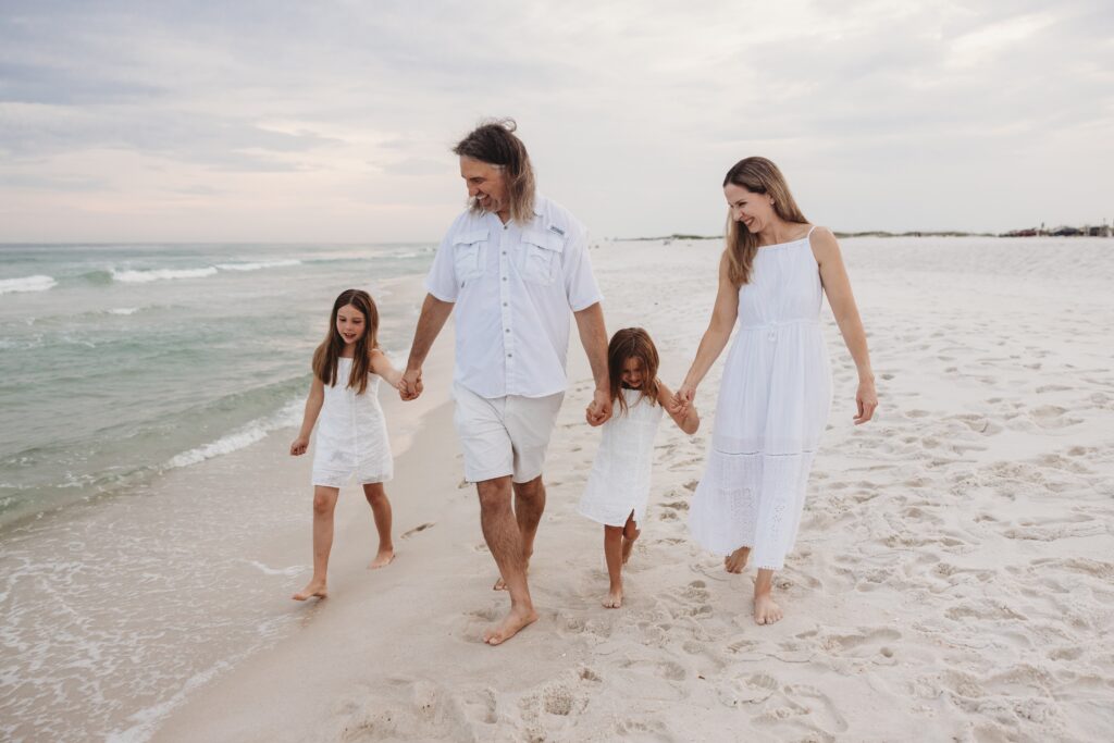 Family of 4 walking down Navarre Beach at sunset. Family photo session by Jennifer Beal Photography. 