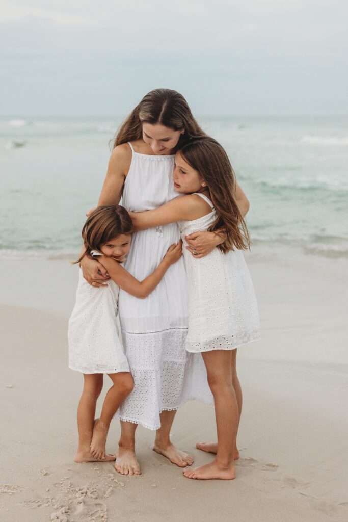 Mother hugging daughters on Navarre Beach during family photo session by Pensacola Family Photographer, Jennifer Beal.
