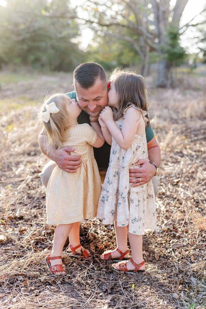 Dad with two daughters giving kisses during photoshoot in a field. Image included in guide to family photos.
