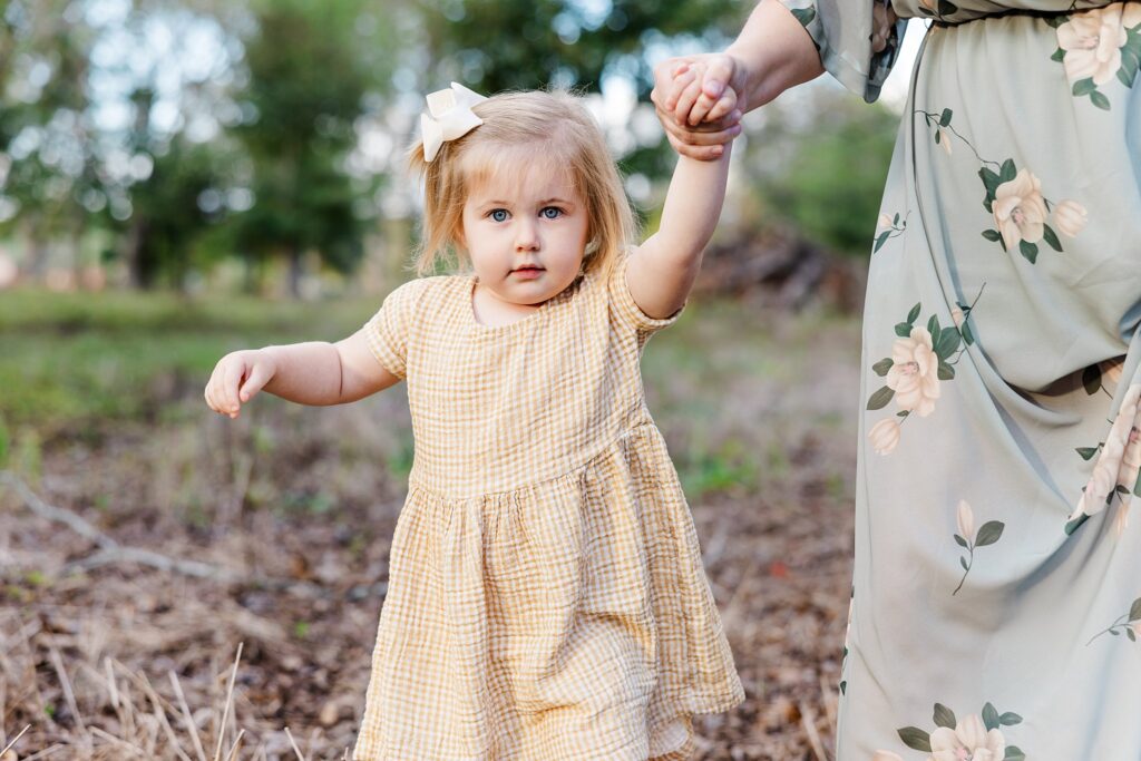 Little girl holding mom's hand during photo session. Shared on a blog post guide to family photos.