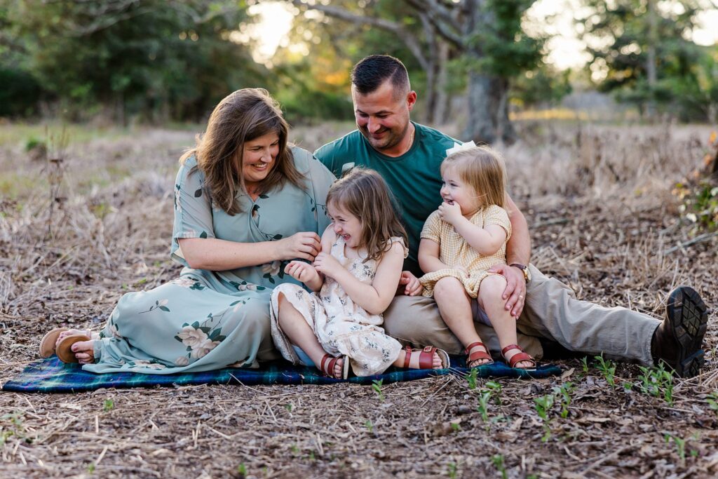 Family of four sitting on the ground in a wooded lot during a photo session.