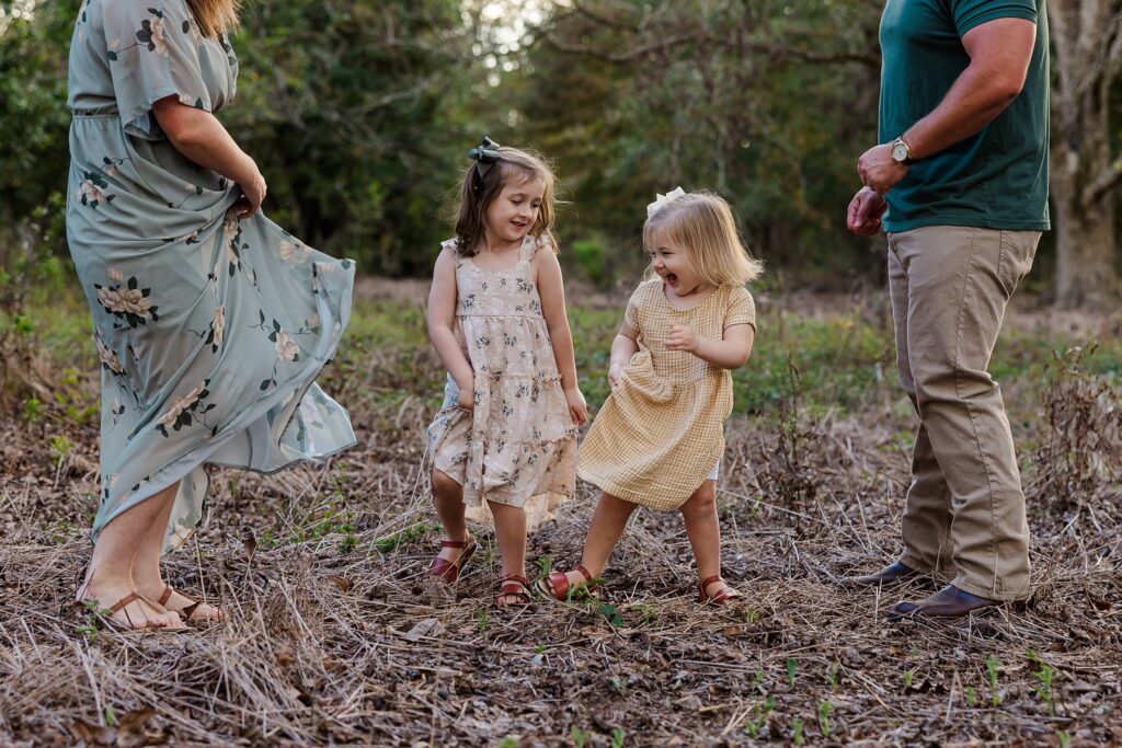 Family of four with two young daughters dancing in a wooded lot during a photo session.