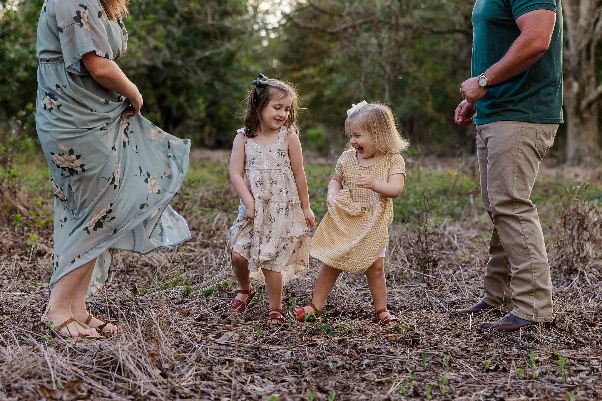 Family of four with two sisters dancing during photo session in a wooded lot.