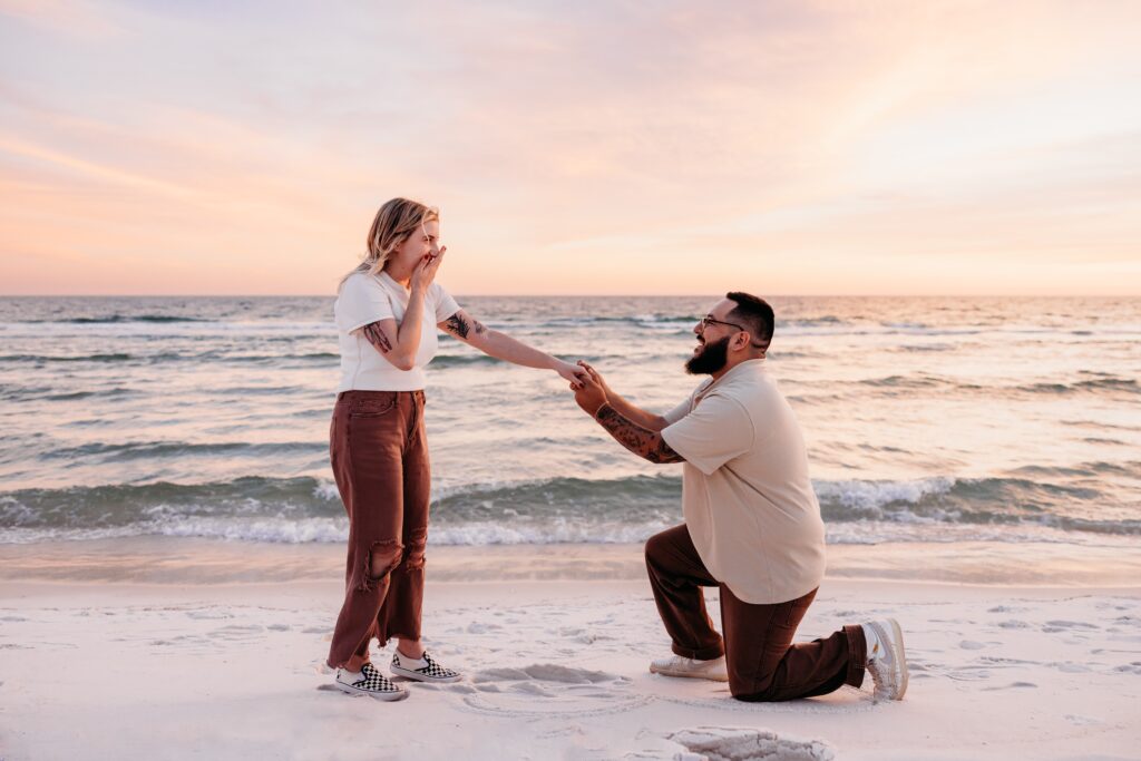 Surprise proposal on Pensacola Beach captured by Jennifer Beal Photography. Young man on one knee proposing to surprised girlfriend. 