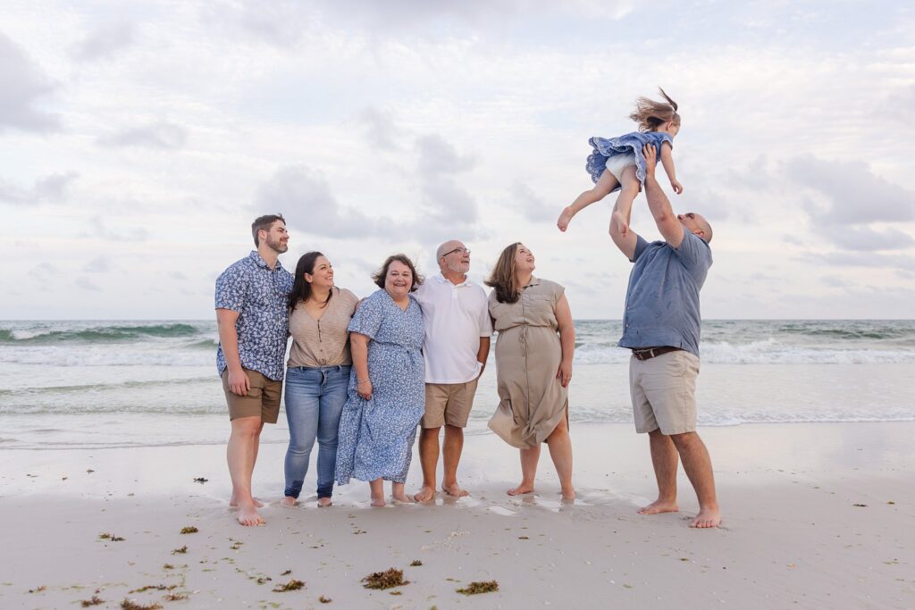 Extended family photo session on Pensacola Beach. Family watching dad toss young daughter into the air.