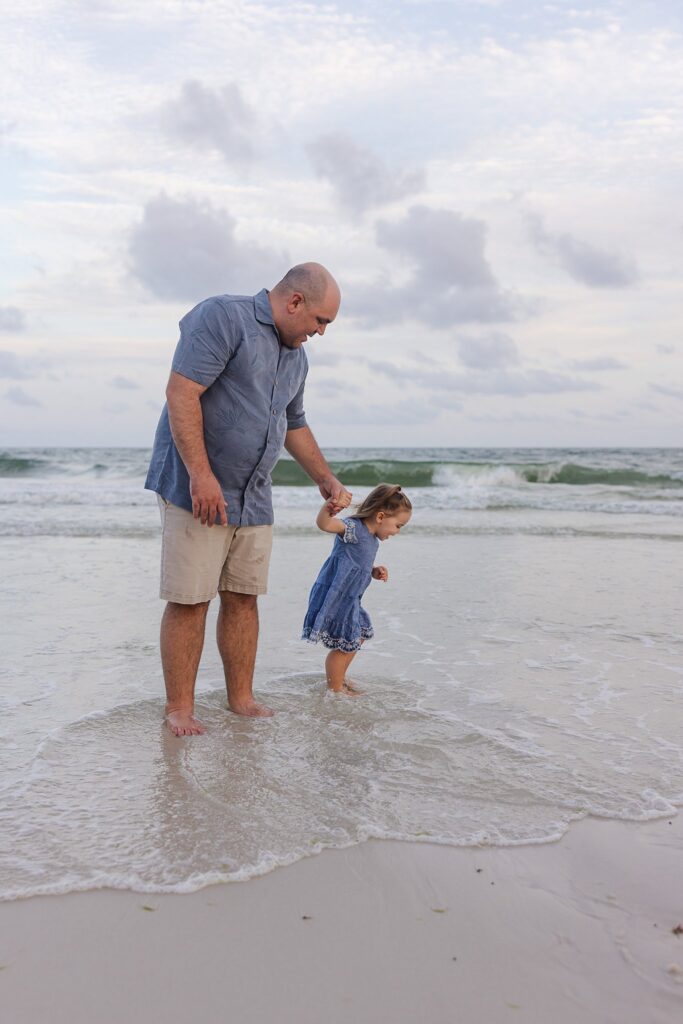 Stress-free family photo session on Pensacola Beach. Dad walking through waves with young daughter.
