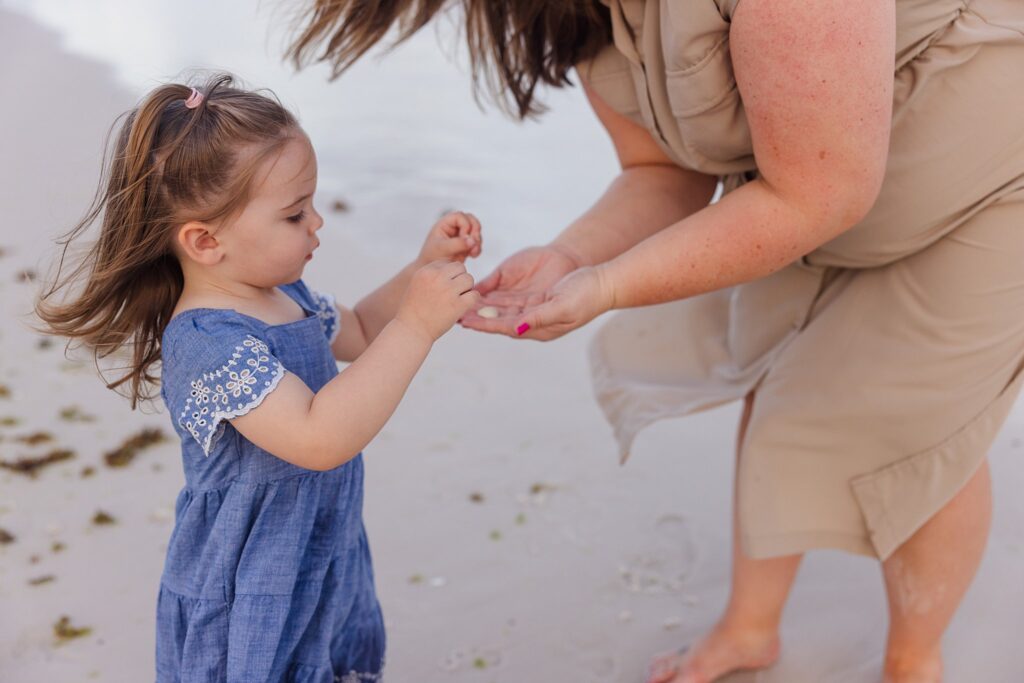 Stress-free family photo session on Pensacola Beach. Young child showing seashells to mom. 